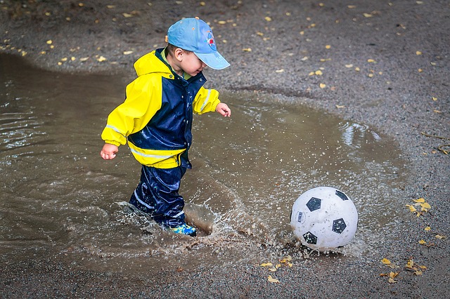 Et barn som leker med ball ute i regnet. 